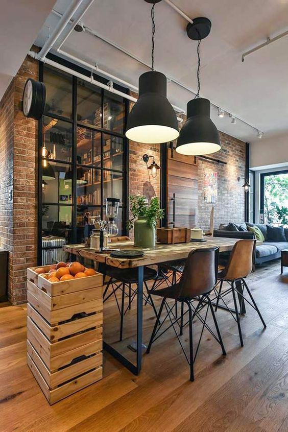 an industrial dining spot with a wood and metal table, cool chairs, crates with fruit, black metal pendant lamps