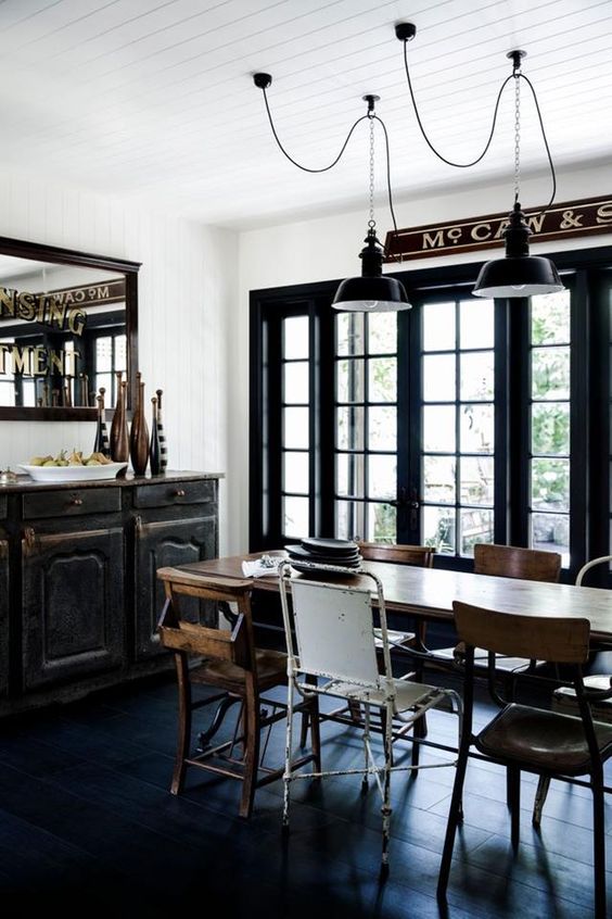 an industrial dining zone with a black vintage credenza, a stained table, mismatching chairs and black metal pendant lamps