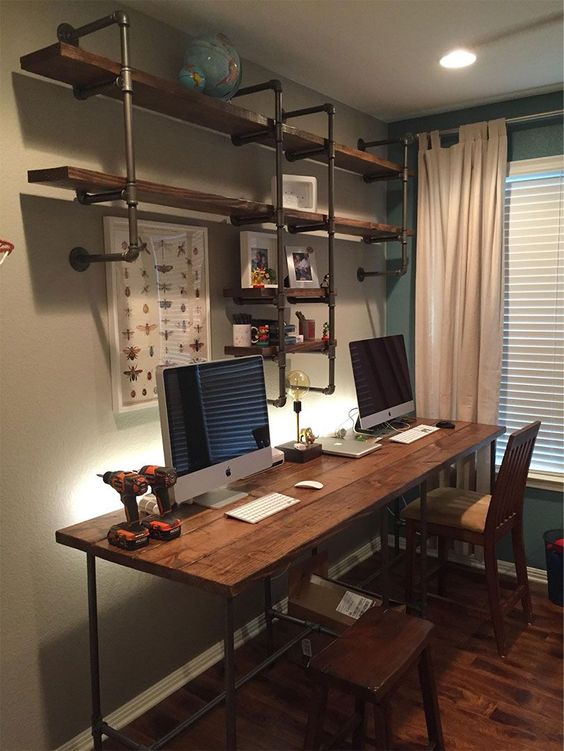 an industrial home office with a pipe and wood shelving unit, a matching desk and wooden chairs, neutral curtains