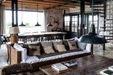 an industrial living space with some sofas and upholstered benches, a wooden coffee table plus retro pendant lamps