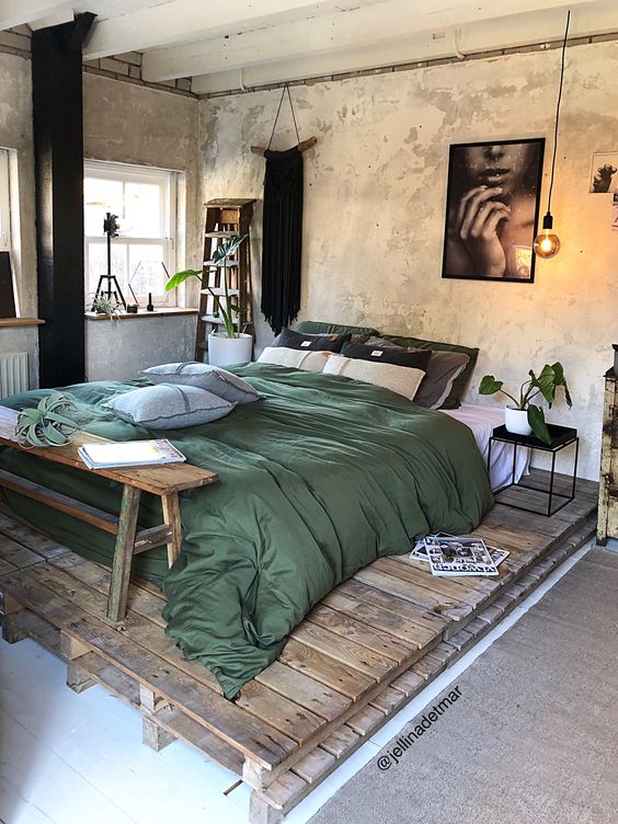 an industrial sleeping space with shabby walls, a pallet platform with a bed, a wooden bench, some pretty plants and textiles