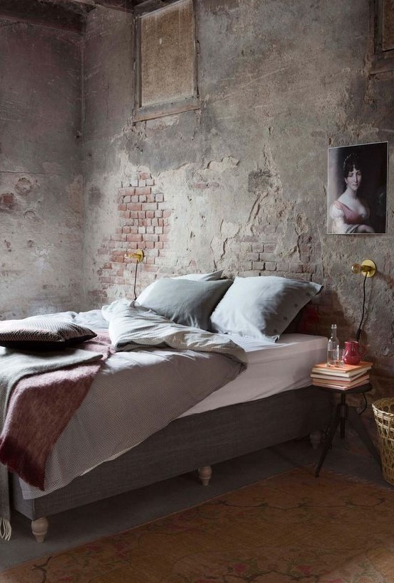 an industrial space with shabby chic brick walls, a grey upholstered bed, a refined artwork and a metal nightstand