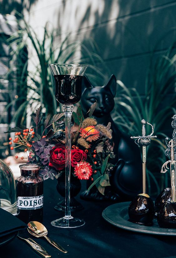 a Halloween tablescape done in black, with a black cat figurine and a bold floral centerpiece with berries and dried touches