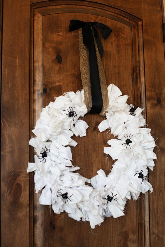 a Halloween wreath covered with white fabric stripes, with black spiders and a burlap and black ribbon is simple and cool