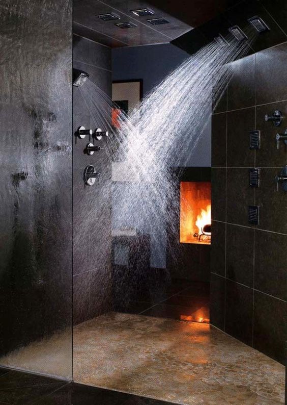 a black and dramatic shower space with stone tiles, a fireplace and rain shower heads on the walls and ceiling