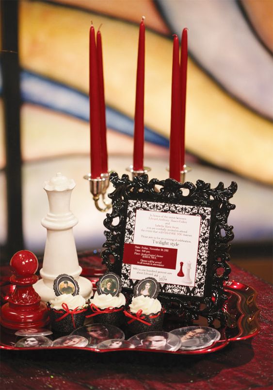 a black and red dessert table with a tray with red candles, chess, cupcakes topped with photos and a refined black frame