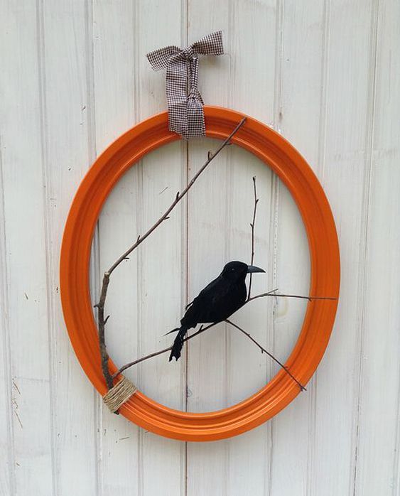 a bright and cool Halloween wreath of an orange picture frame, branches and a blackbird is a lovely and bold idea to rock
