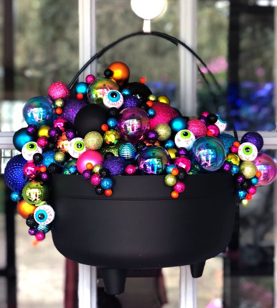 a cauldron with lots of bright and gltiter ornaments and eyeballs is a gorgeous Halloween decoration