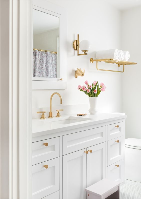 a chic white bathroom with gold fixtures, a gold shelf, a gold sconce is a very stylish and cool idea to rock