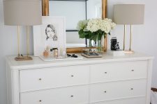 a chic white dresser with gold knobs, a mirror with a gilded frame, table lamps with gold bases is amazing