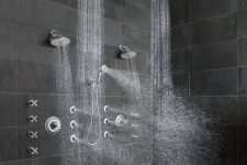 a contemporary shower space with large scale grey stone tiles, a dark stone chevron floor, rain shower heads on the ceiling and some on the wall