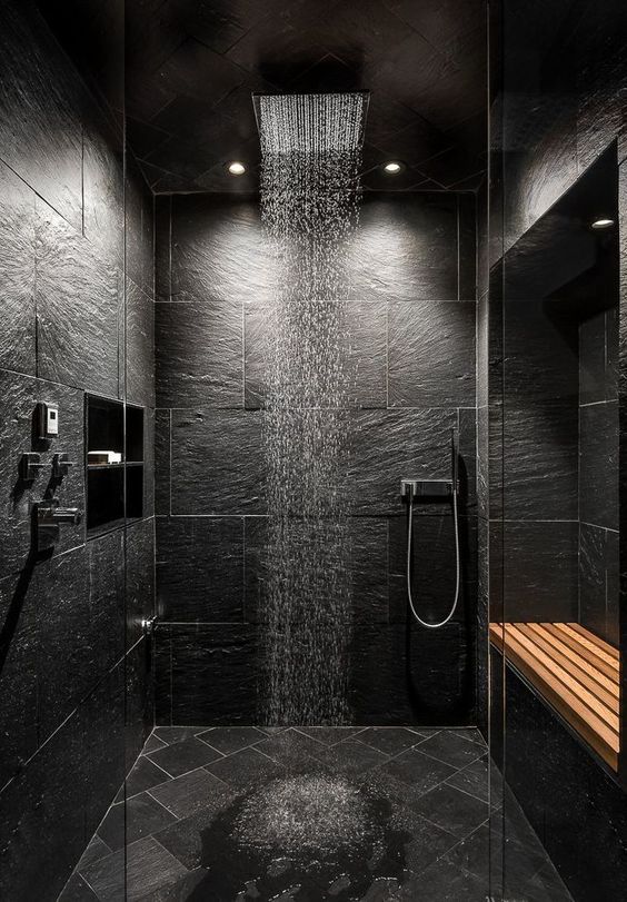 a dramatic black stone bathroom with tiles on the floor, stainless steel fixtures and a shower head plus built-in lights