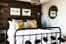 a farmhouse bedroom with a dark-stained accent wall, a black metal bed with neutral bedding, wall sconces and a woven lamp