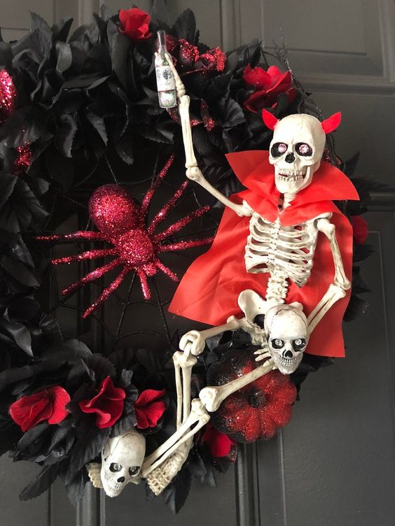 a fun Halloween wreath of black and red fabric blooms, a red glitter spider and pumpkins, a skeleton dressed in a red trench