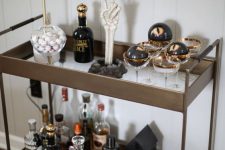 a glam Halloween bar cart with gold rimmer glasses, black eyes, a lamp and spider print plates