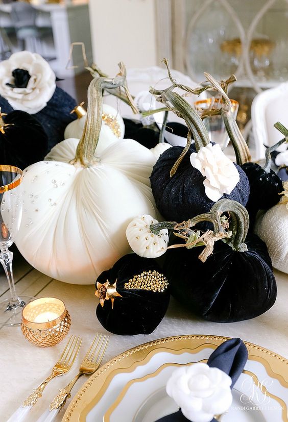 a glam Halloween centerpiece of black and white pumpkins with beads and studs, gold candleholders and chargers