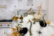 a glam Halloween centerpiece of white and black pumpkins with spiders, gold leaves and white blooms