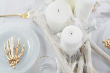 a glam Halloween table setting done in white, with bones, gold skeleton hands, candles and spiderwebs