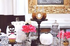 a glam Halloween table with a black sequin tablecloth, gold chargers and skeletons, pink blooms and white pumpkins