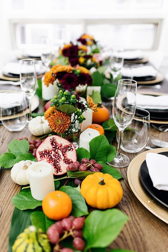 a lush table runner of foliage, berries, fruits, blooms, pillar candles and mini pumpkins for a Thanksgiving table