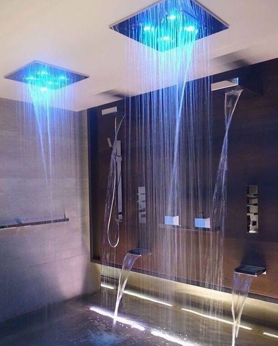 a luxurious shower space with waterfalls and waterfall and rain shower heads with regulated color lights