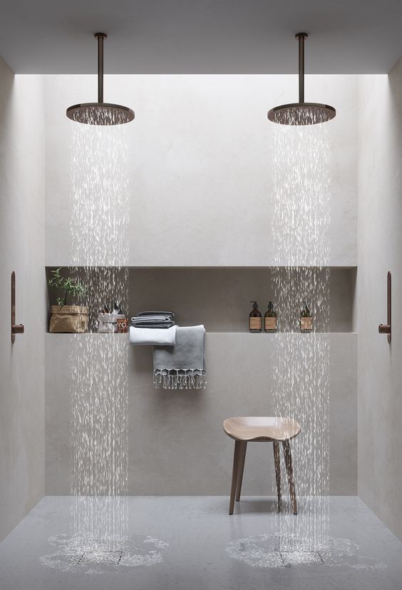 a minimalist bathroom done with neutral stone, with a niche shelf for storage, rain shower heads and a wooden stool