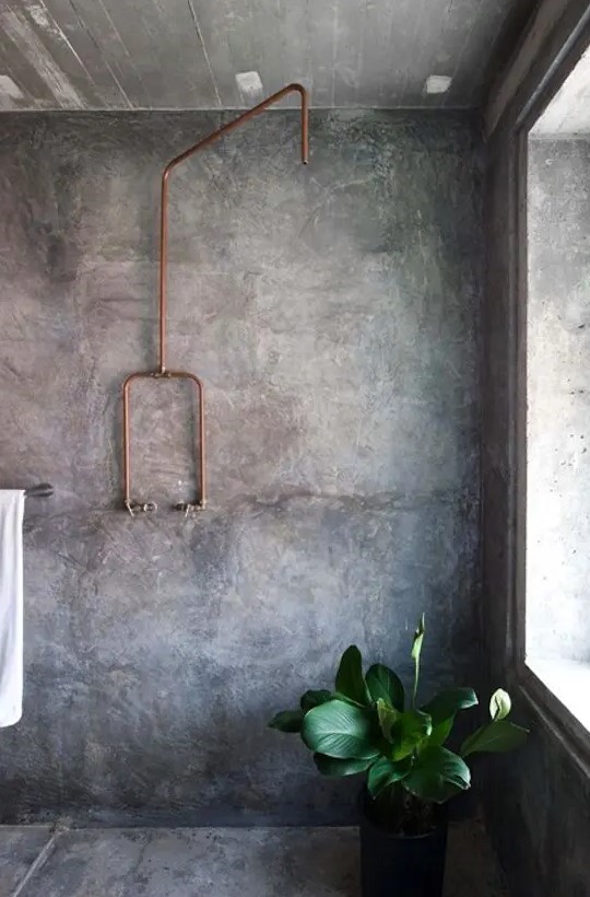 a modern industrial bathroom with concrete walls and a floor, an exposed copper pipe and potted plants is a chic and functional space