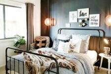 a modern industrial bedroom with a black accent wall, a black metal bed, neutral and printed bedding, a woven rug and a gallery wall
