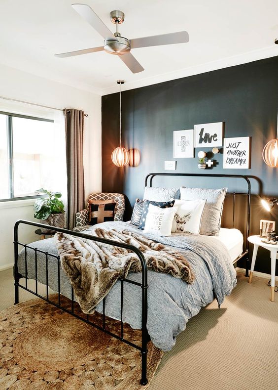 a modern industrial bedroom with a black accent wall, a black metal bed, neutral and printed bedding, a woven rug and a gallery wall
