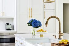 a modern white kitchen with a farmhouse feel, gold fxitures and handles, gold pendant lamps on chains is very chic and stylish
