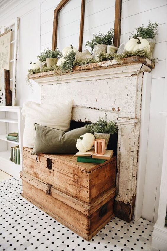 a neutral and relaxed fall fireplace with pillows and greenery, white pumpkins and cocnrete pots for a vintage feel