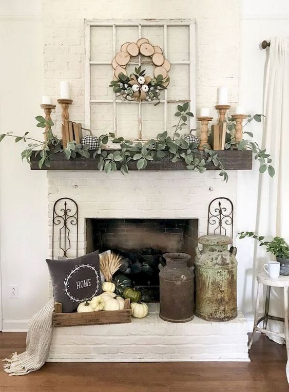a neutral fall fireplace wwith shabby chic churns, white pumpkins and wheat, wooden candle holders and much greenery