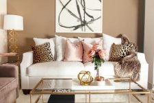 a neutral to muted living room with a white sofa, printed pillows, a printed artwork, a table lamp and a dusty pink sofa