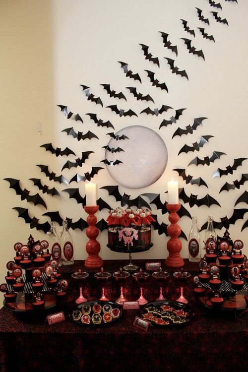a red and black Halloween dessert table surrounded with black bats, with red candleholders, red and black desserts