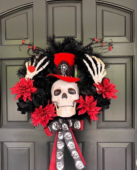 a red and black Halloween wreath of fabric blooms, feathers, branches, skeleton hands and a skull wearing a top hat