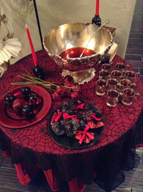 a refined drink station with a black and red spiderweb tablecloth, black and red plates, an exquisite punch bowl and red candles
