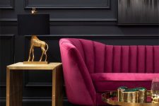 a refined living room with black paneled walls, a fuchsia loveseat, a gold table and a gold side table, gold and black table lamp