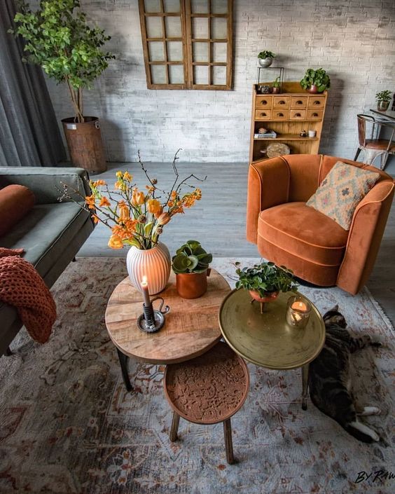 a rust-colored chair, blanket, bright coffee tables and bold orange blooms add fall coloring to the living room