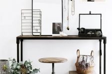 a small and pretty industrial working space with a metal console table, a metal pipe and wood stool, various jewelry on stands and some decor