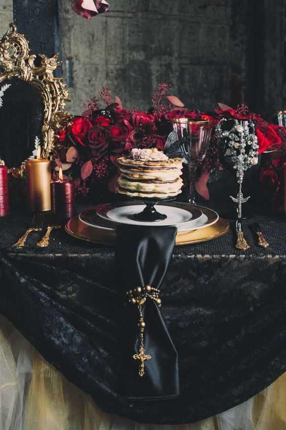 a sophisticated Halloween tablescape with plenty of burgundy and red blooms, burgundy and gold candles, gold chargers and cutlery
