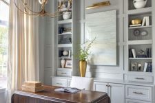 a sophisticated vintage-inspired home office with light grey cabinets, a dark stained desk, delicate gold touches – a chandelier, a lamp, a vase and pillows