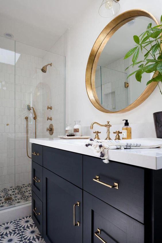 a stylish bathroom with white and mosaic tiles, a navy vanity with a white countertop, a mirror in a gilded frame, gold fixtures is very chic