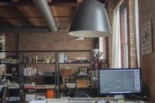 a stylish industrial home office with red brick walls, a comfy desk and a black chair, a metal shelving unit, exposed pipes and metal pendant lamps
