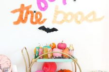a super bright bar cart filled with colorful pumpkins and paper balls, colorful barware and with letters above