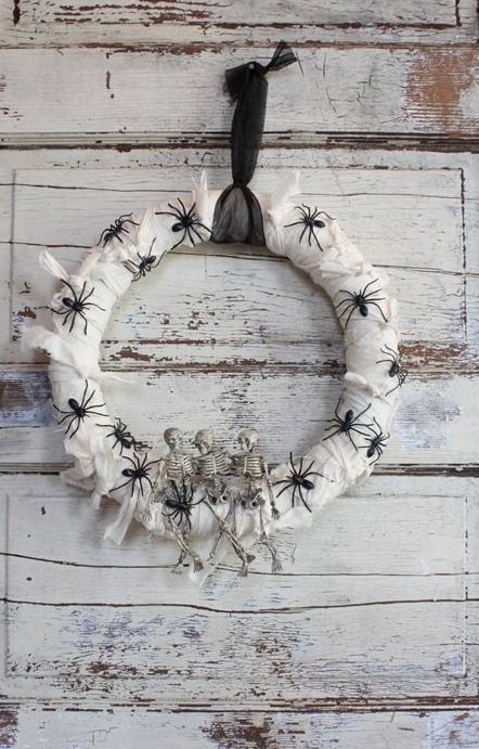 a white wrapped Halloween wreath covered with black spiders, skeletons and a black ribbon is a pretty and simple idea