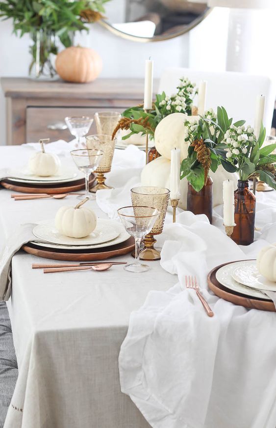 an elegant Thanksgiving table with wooden chargers, candles, amber glasses and apothecary bottles plus white pumpkins