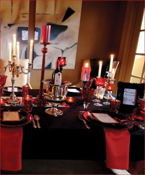 an elegant black and red vampire-inspired Halloween tablescape with red candles and napkins, with black plates and metallic candelabras