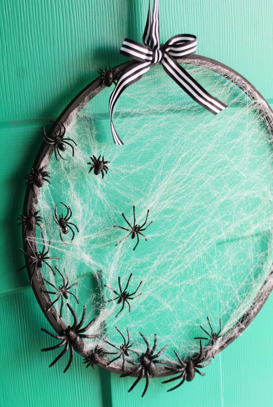 an embroidery hoop Halloween wreath with spider net and small black spiders plus a striped bow is easy to DIY