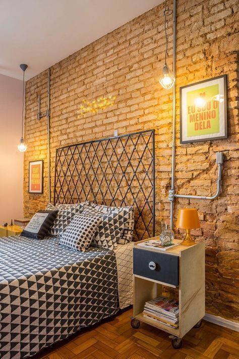 an industrial bedroom with a brick accent wall, a bed with a statement metal headboard, exposed pipes and plywood nightstands