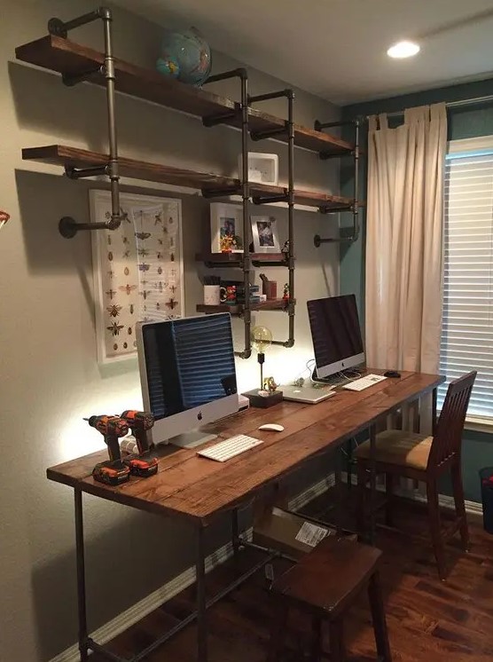 an industrial home office with a pipe and wood shelving unit, a matching desk and wooden chairs, neutral curtains